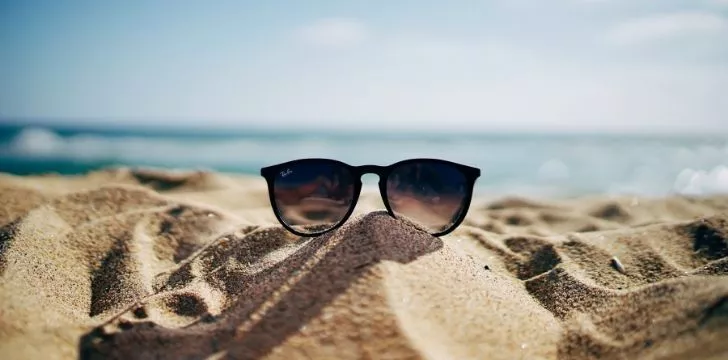 Чифт слънчеви очила Ray Ban върху пясък на плажа с океана зад тях