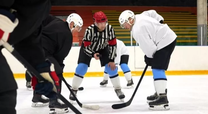 Хокейният съдия държи шайбата между двама играчи.