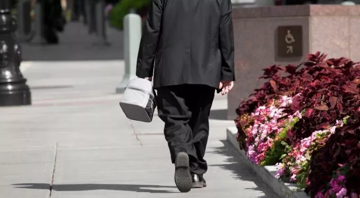 Човек в костюм върви по главната улица с кутия за обяд