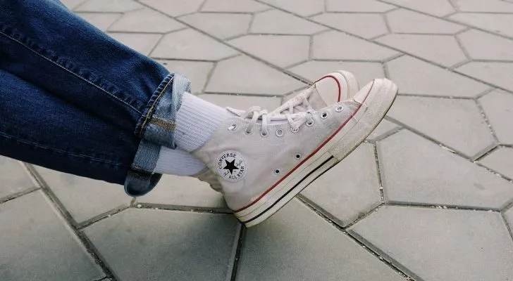 Кръстосани крака, обути в бели обувки Chuck Taylor Converse