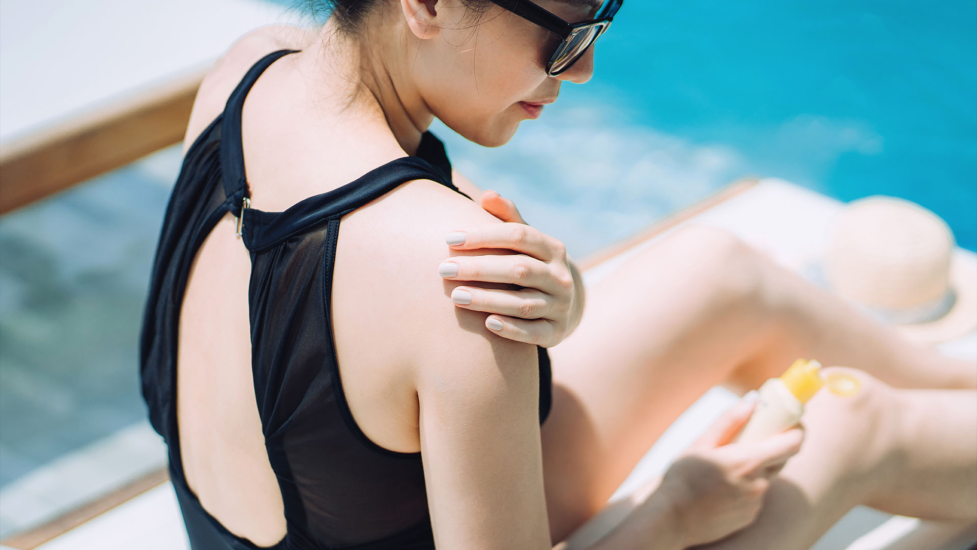 Млада жена, нанасяща лосион за загар, докато се слънчеви бани край басейна.