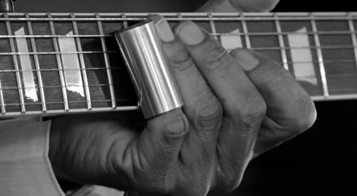 Ръка, свиреща на китара с метален цилиндър, покриващ единия пръст