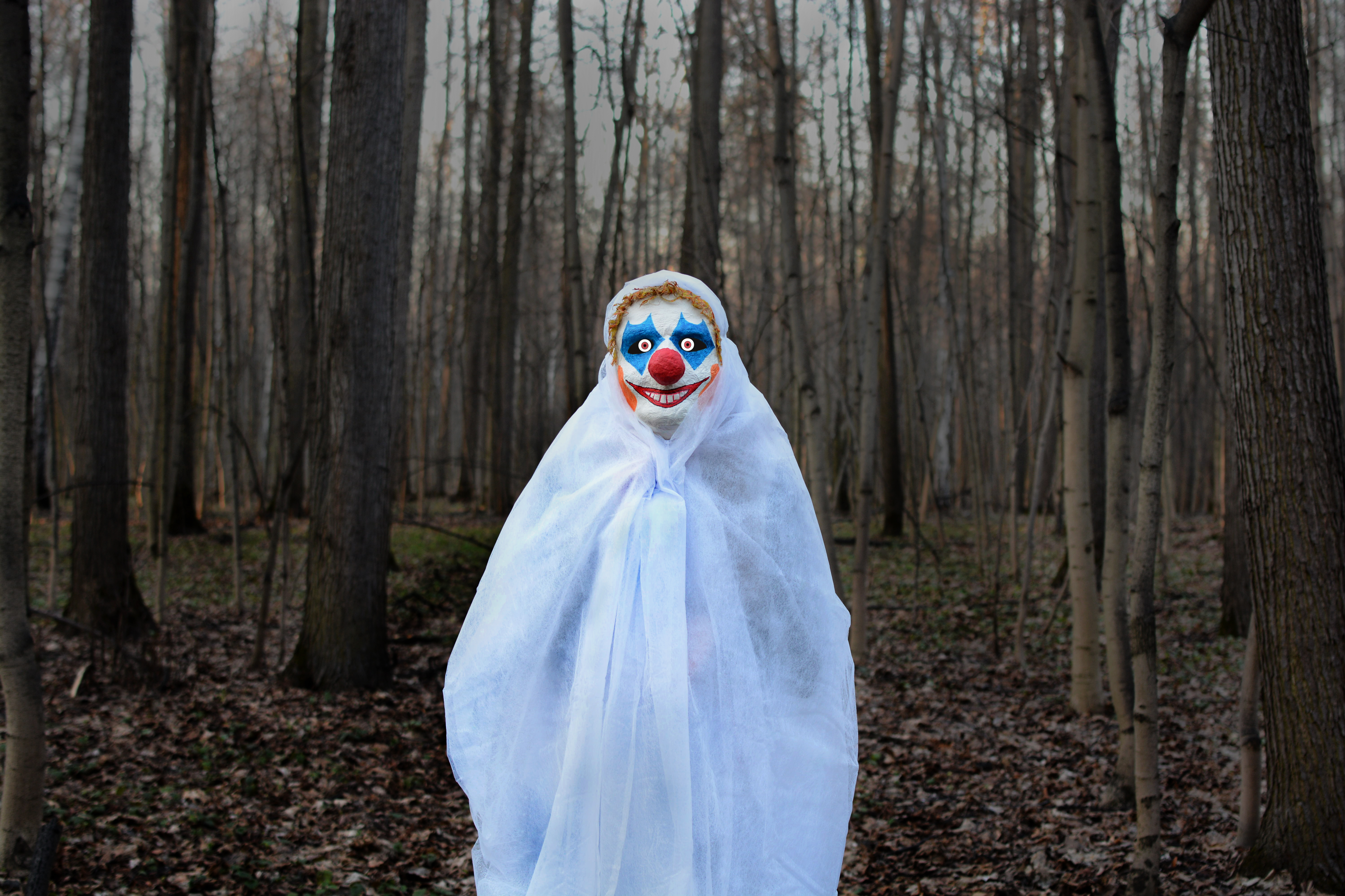 Човек, облечен като страшен клоун в гората с бял чаршаф.