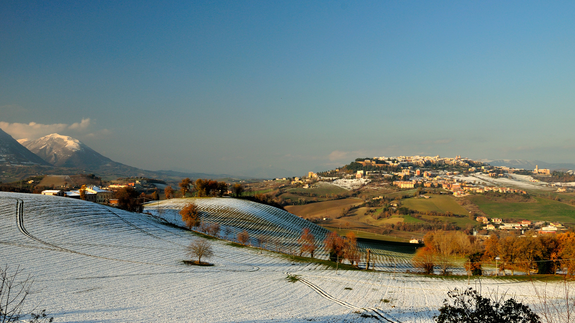 Снимка на град Камерино в Апенинските планини в Италия със сняг по хълма и града в зелената долина отдолу.