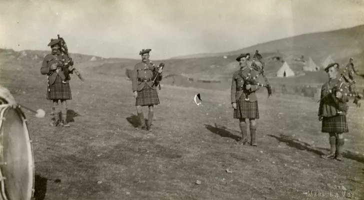Four soldiers play bagpipes while wearing kilts