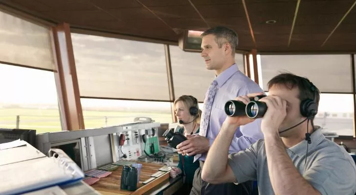 Three air traffic controllers look out over an airport