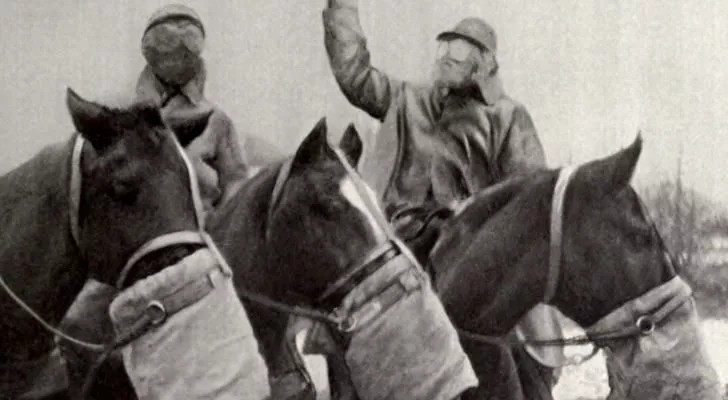 Three horses wearing gas masks carry their riders who also wear gas masks
