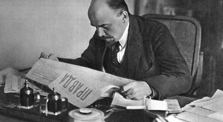 Vladimir Lenin sits at a desk and reads a Russian newspaper