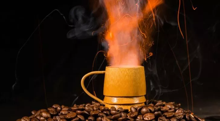 A cup sits on a pile of coffee beans while a fiery column shoots up out of it