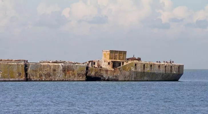 A large concrete ship sits derelict in the sea