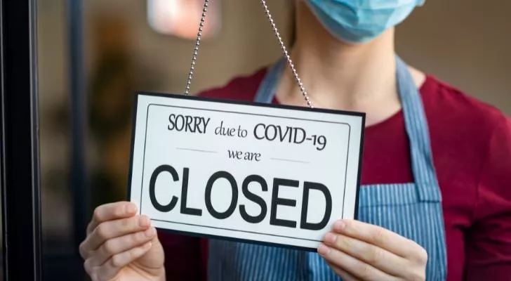 Жена с маска поставя табела „затворено поради COVID-19“ на прозореца