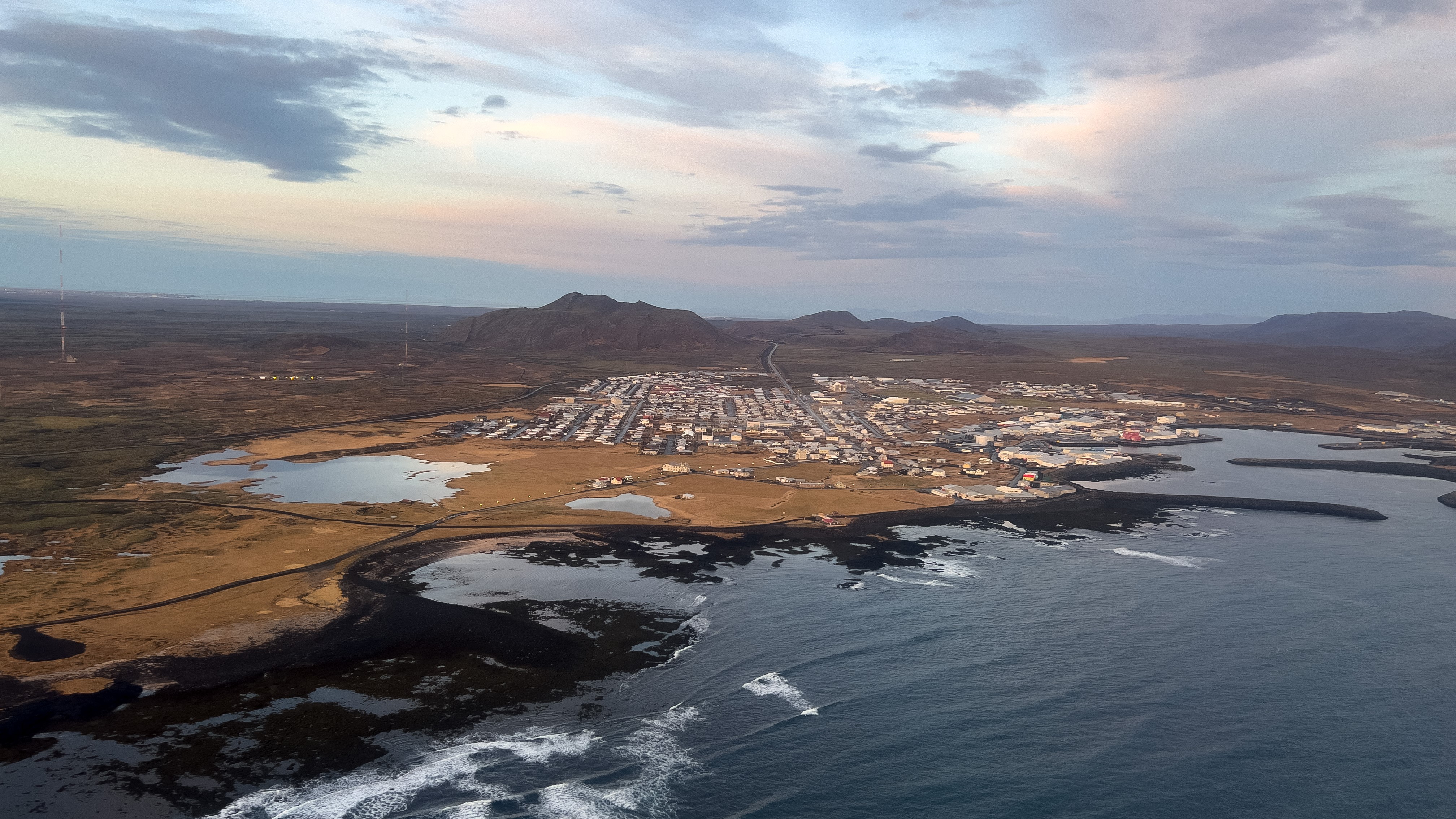 исландският град Гриндавик с морето на преден план и хълмове на заден план