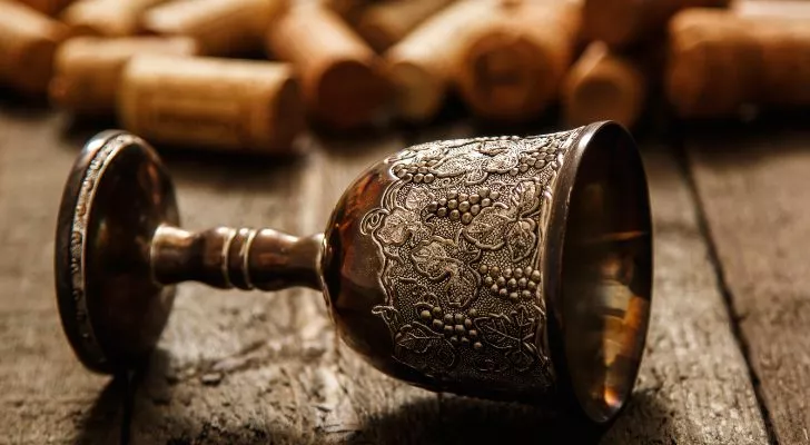 Чаша за вино в средновековен стил лежи настрани върху маса, заобиколена от тапи