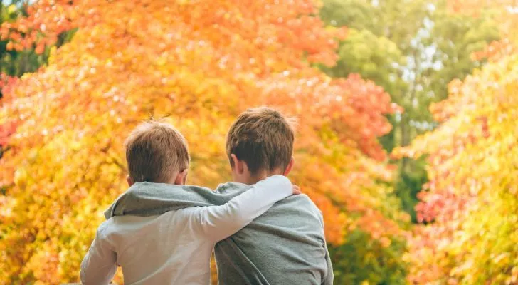 Две млади момчета с прегърнати ръце пред дърво през есента