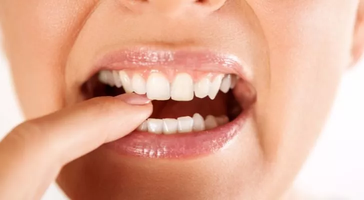 Една жена пъха пръст между зъбите си и го държи там със зъбите си