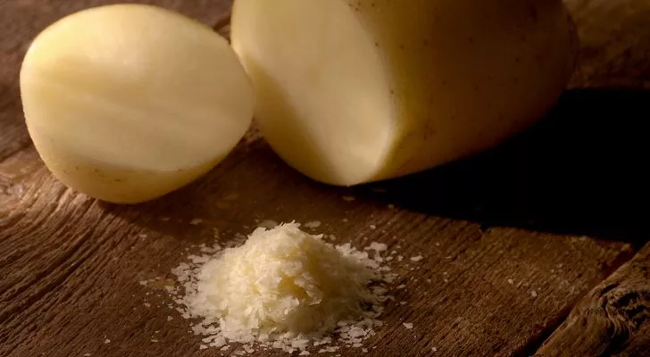 Две нарязани парчета картофи върху дървена маса отстрани на люспи от картофа