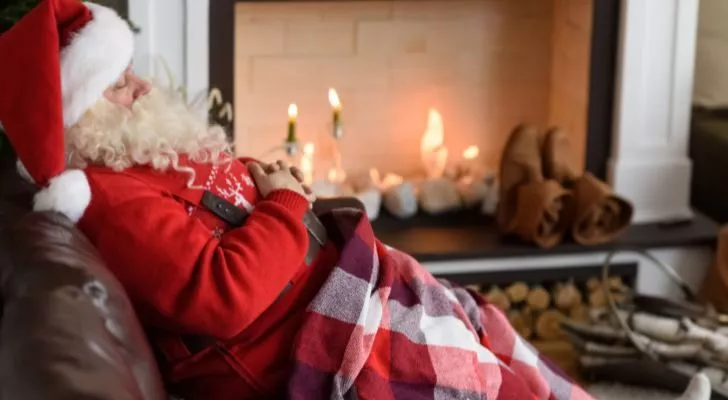 Дядо Коледа спи на стол пред камина, покрит с одеяло