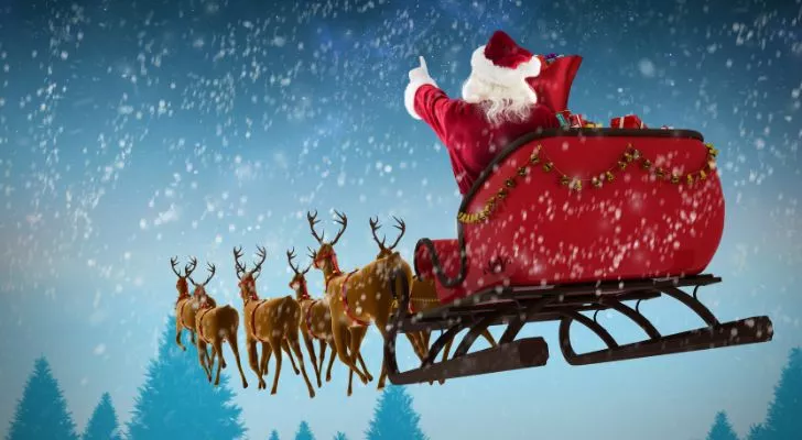 Дядо Коледа кара шейната си през заснежено небе, воден от летящи северни елени