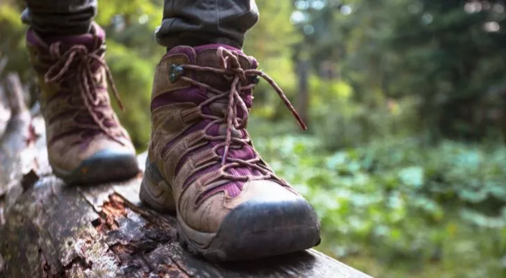 Човек в туристически обувки върви по дънер в гора