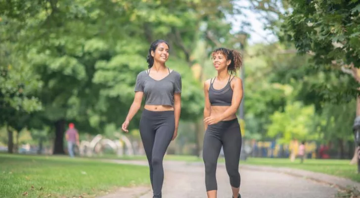 Две жени в спортно облекло вървят през парк