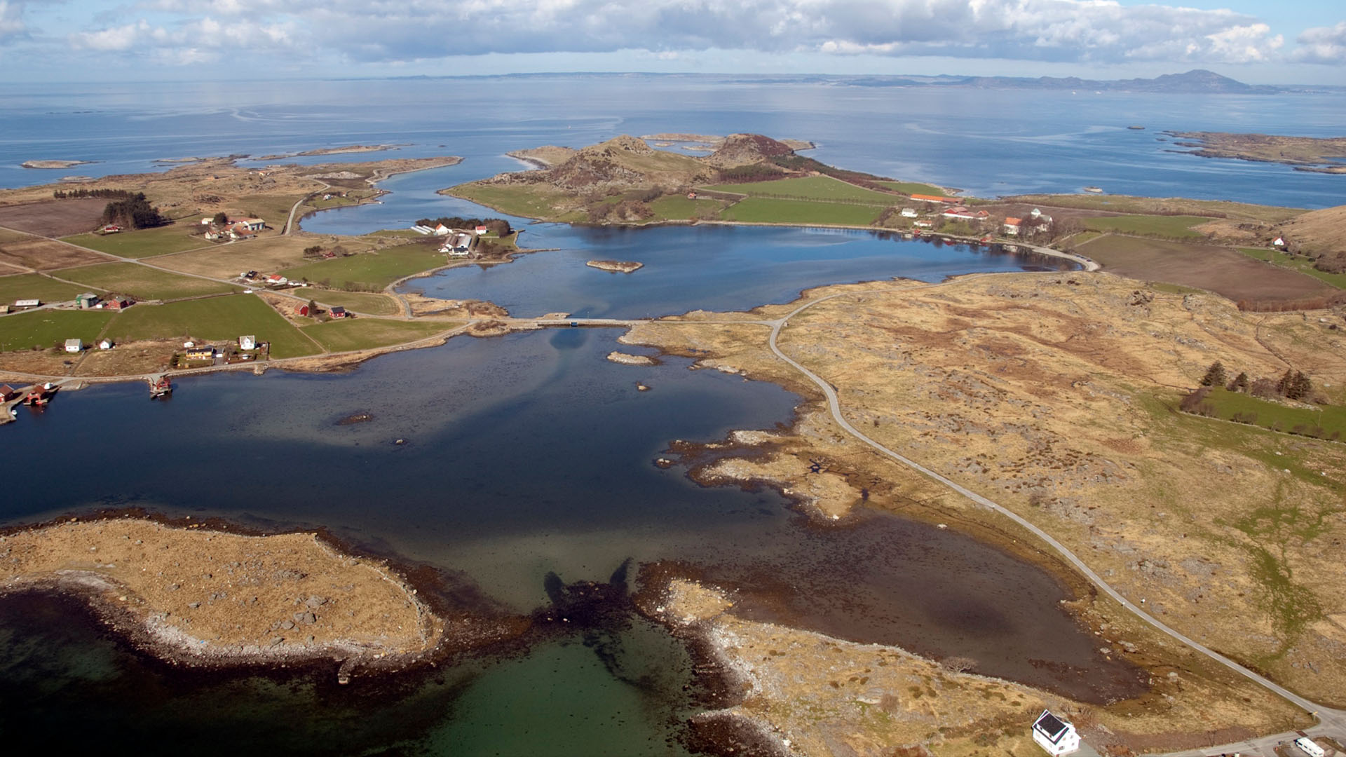 Островно село в Норвегия със зелени полета, заобиколено от вода.