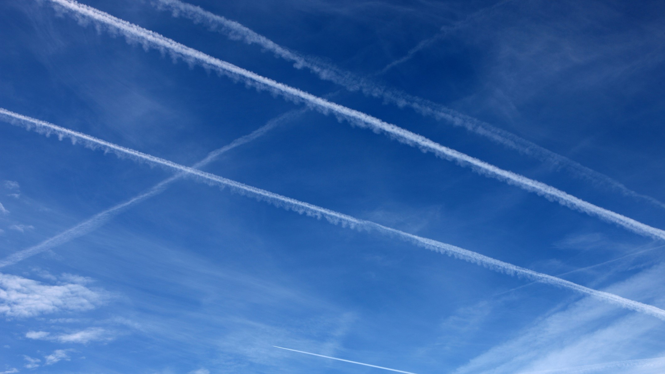 Синьо небе с няколко обратни следи, маркиращи траекториите на полета на самолетите.