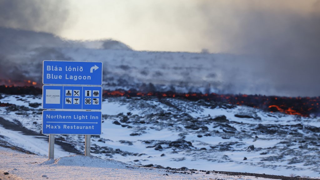 Пътен знак, сочещ към курорта Blue Lagoon и Northern Light Inn в Svartsengi, стои на преден план сред поток от лава.