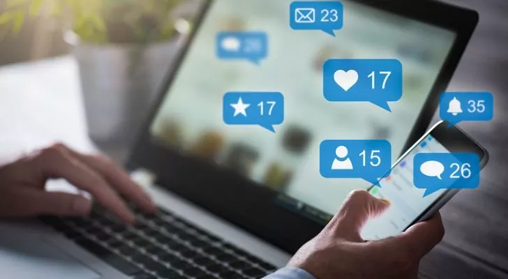 Човек използва лаптоп и телефон с множество икони на социални медии