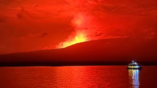 Лава, светеща в червено в нощното небе, докато вулканът изригва