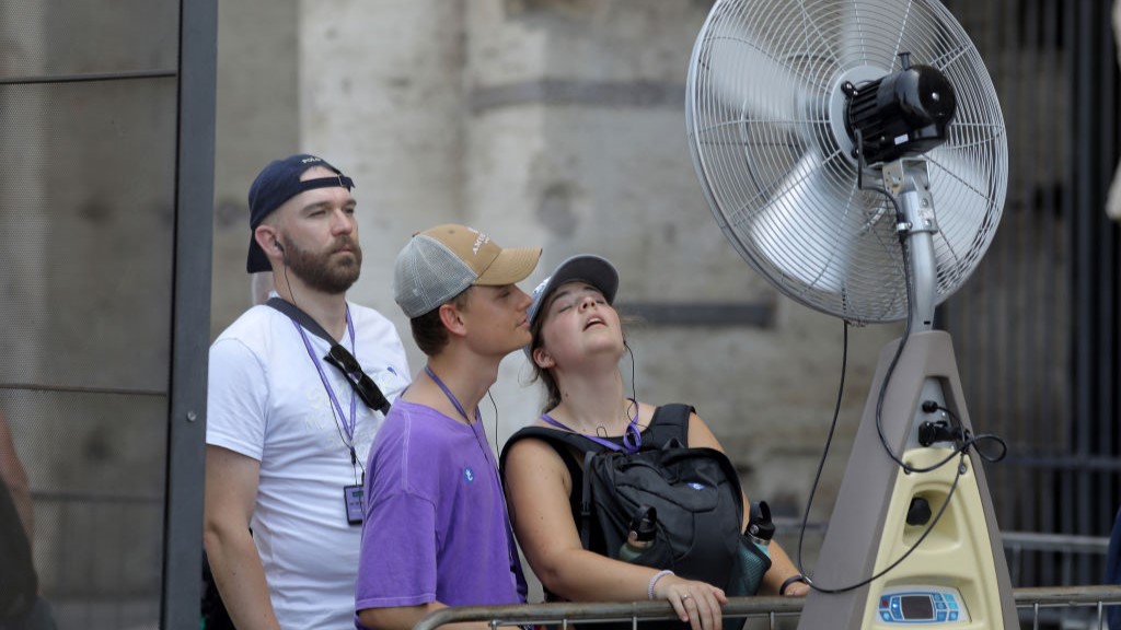 Трима туристи стоят близо до вентилатор, пръскащ небулизирана вода през лятото на 2023 г. в Рим, Италия.