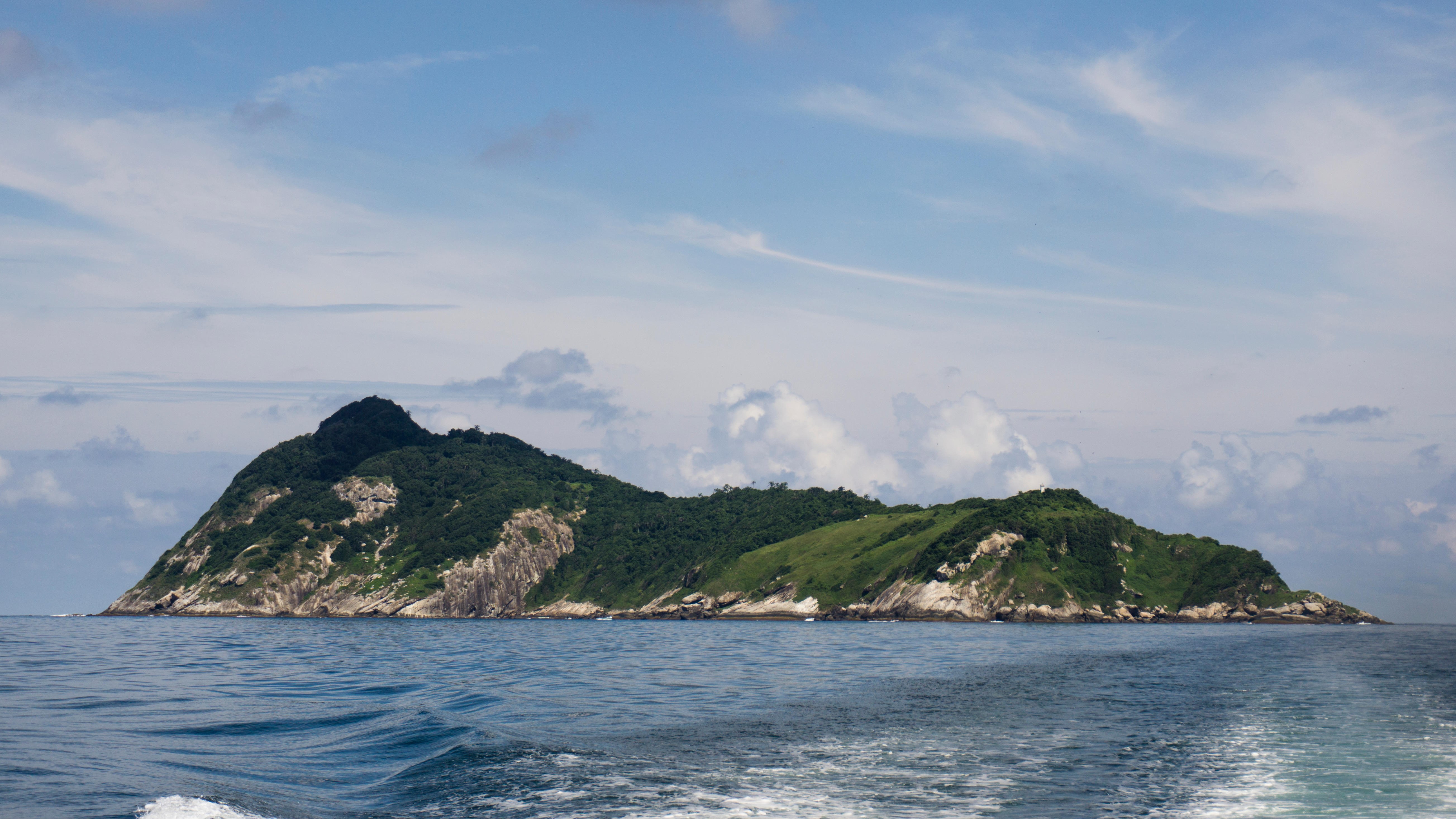 Снимка на Змийския остров, направена от лодка в Атлантическия океан.  Островът има променлив терен от гори, пасища и безплодни скали.