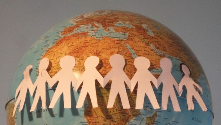 Хартиени изрезки на хора, държащи се за ръце, увити около глобус.